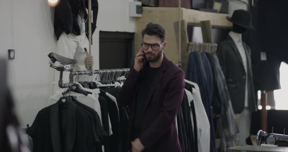 A man browses through shirts on a rack at a clothing store before answering a call on his cell phone and walking away from the rack