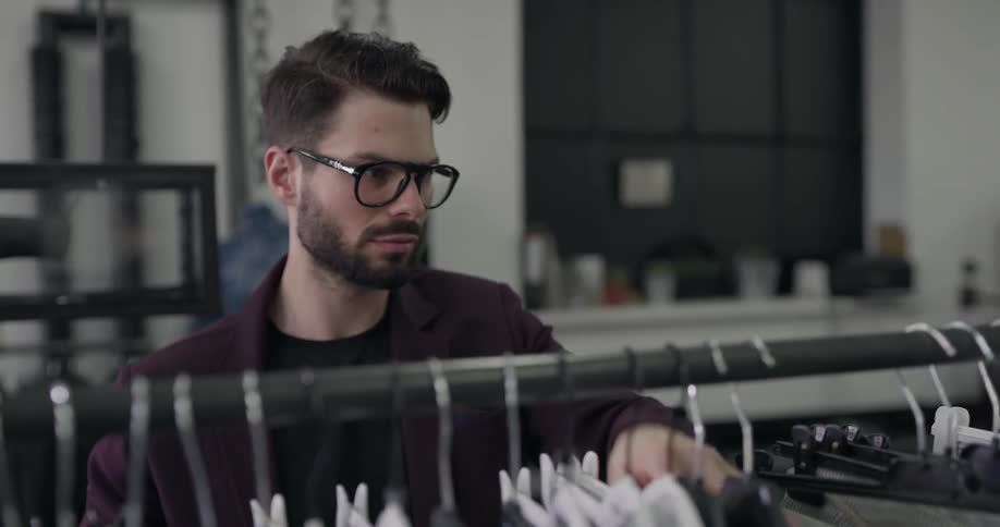 A bespectacled man organizes a rack of clothing in daylight