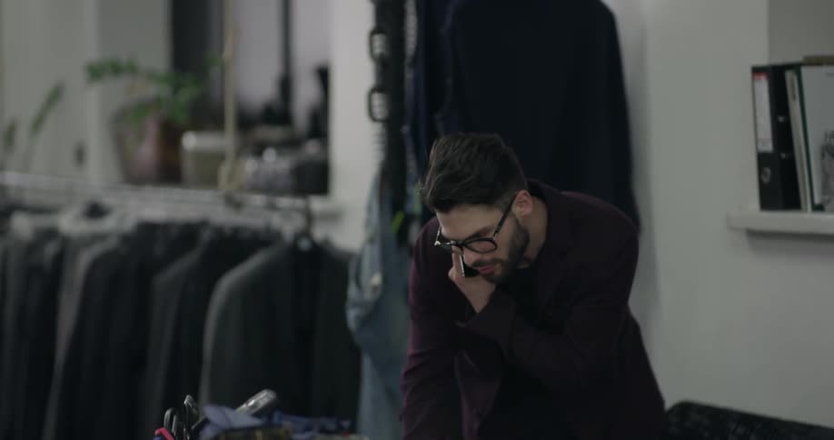 Man wearing blazer and glasses talk on a smart phone in clothing store during daylight