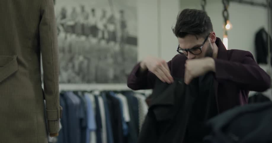 A bespectacled man in a clothes shop folds a t shirt