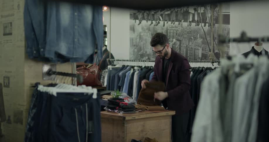 A well dressed man folding clothing in a store