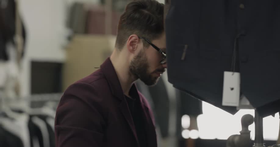 A sales person organizes a rack of apparel and pulls out a vest to look at before putting hanging it back up in a retail store