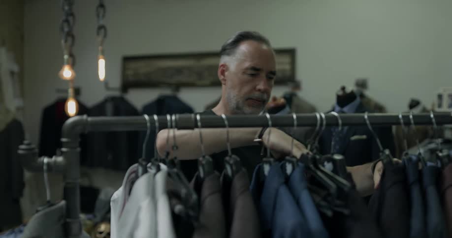 A man picks up clothes from an rack and puts them back