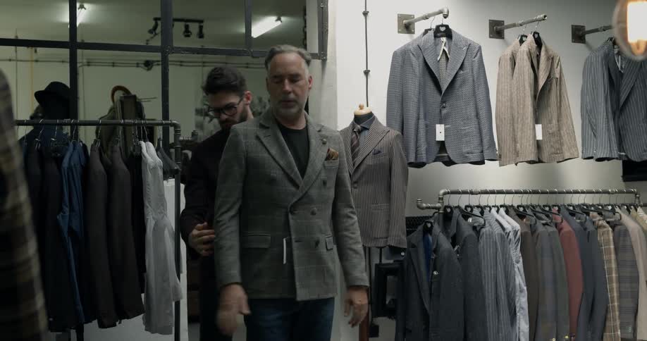 A clothing store professional helps a man try on a jacket in the store