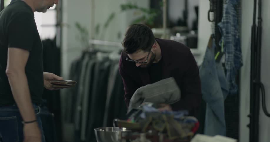 A man folds a blazer for a customer in a clothes shop and shakes his hand