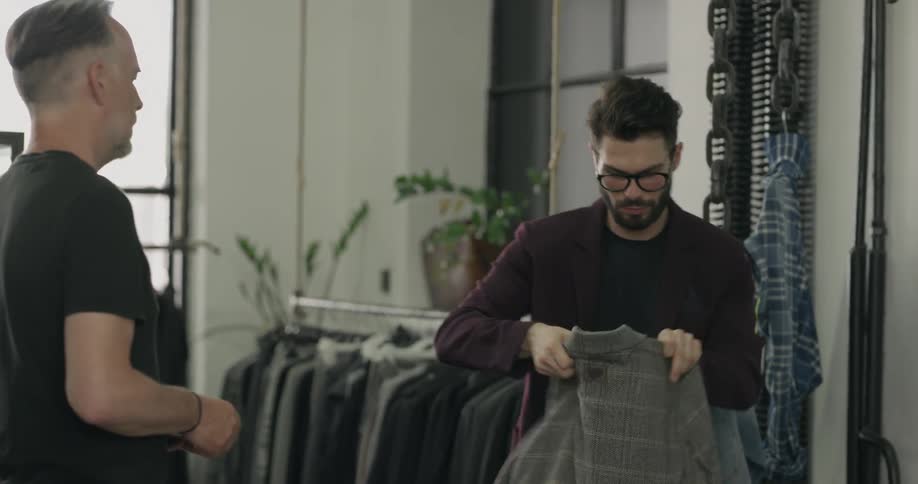 A salesperson gives a customer his receipt before putting a suit jacket in a bag and handing it to him