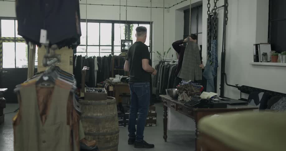 Inside of a men's clothing store and tall man finalizes the purchase of his clothing and the other man as store employee bags it up and hands it to him