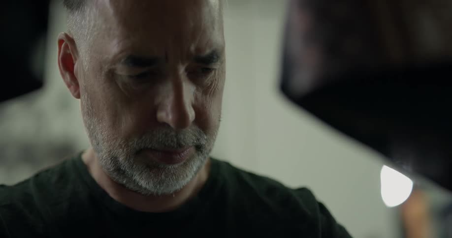 Bald middle aged man wearing black shirt looks down indoors