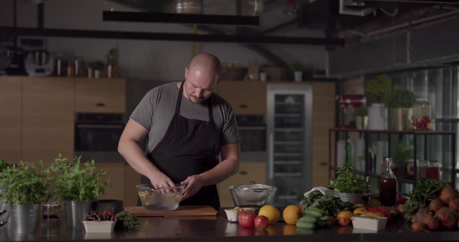 A white man mixes food in a bowl of ice water with his hand and then moves it to a strainer in a large kitchen