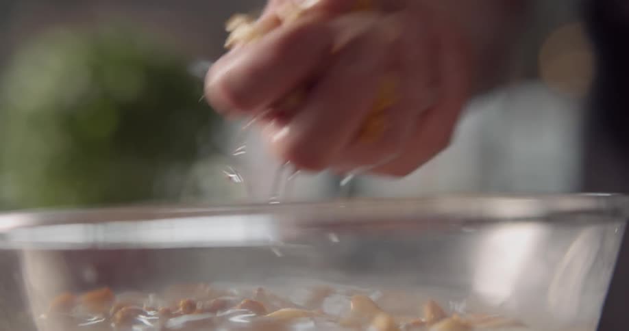 A hand is seen mixing around and washing some mushroom in a glass bowl filled with water and ice