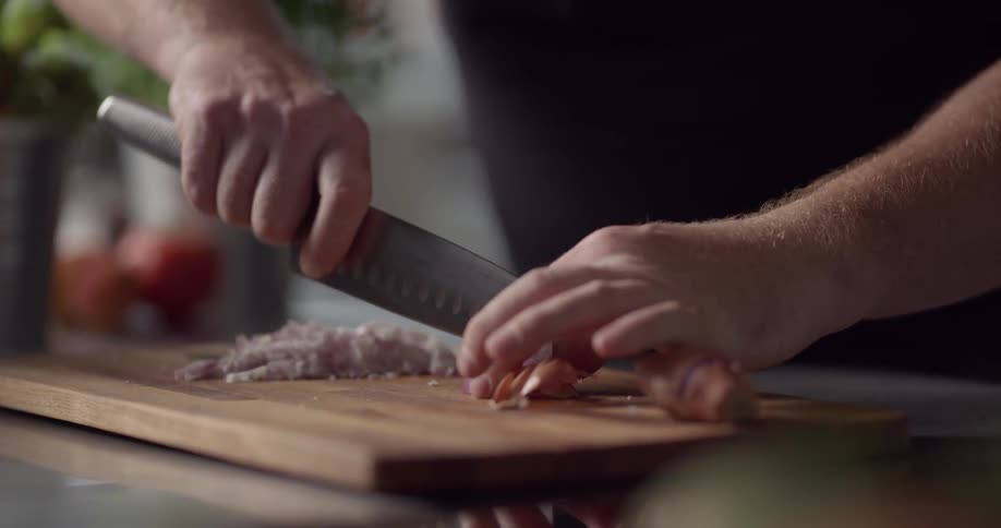Man cuts shallot on cutting board with knife in the kitchen during daylight