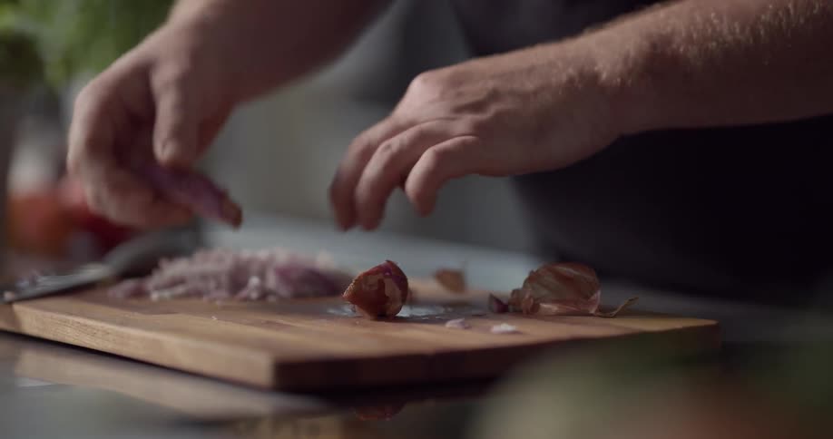 Man peels shallot and cuts on the cutting board in the kitchen during daylight