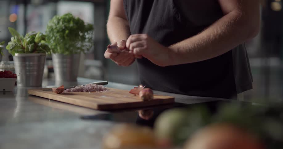 A white man in an apron slices and peels apiece of garlic on wood cutting board in a kitchen