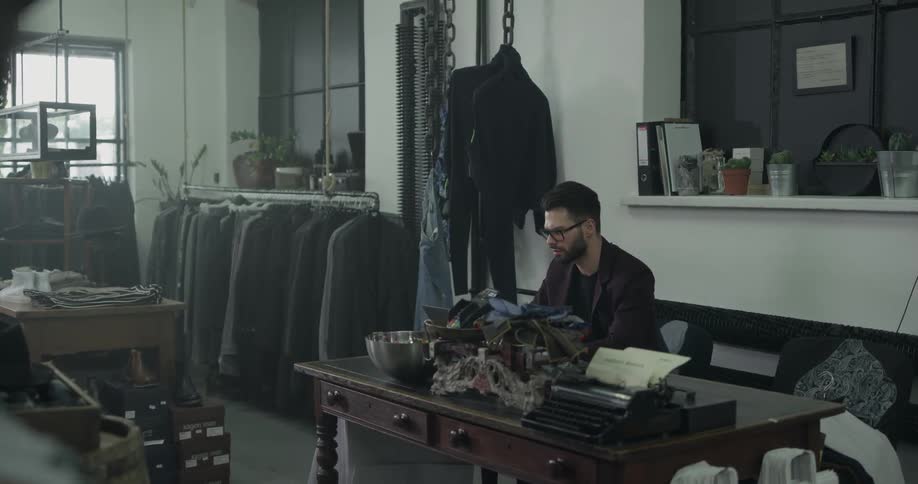 Man wearing blazer and glasses opens desk drawer and puts a piece of paper into it at the clothing store during daylight
