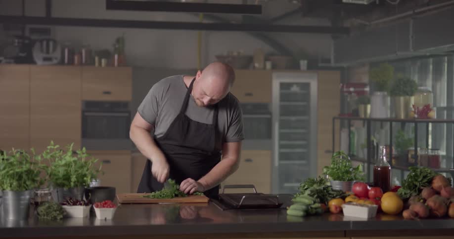A man wearing an apron chops kale on a cutting board in a kitchen