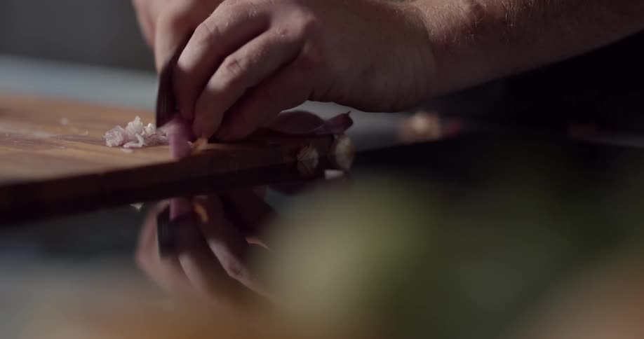 Man chops shallot on the cutting board in the kitchen during daylight