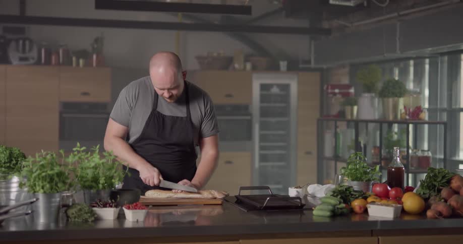 A man slicing a baguette with a knife on a chopping board