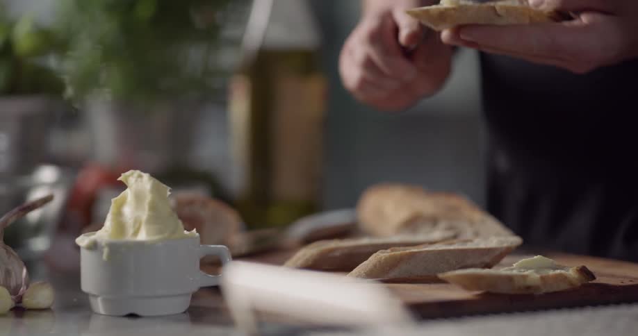Man spreads butter on slices of bread with spoon in the kitchen during daylight
