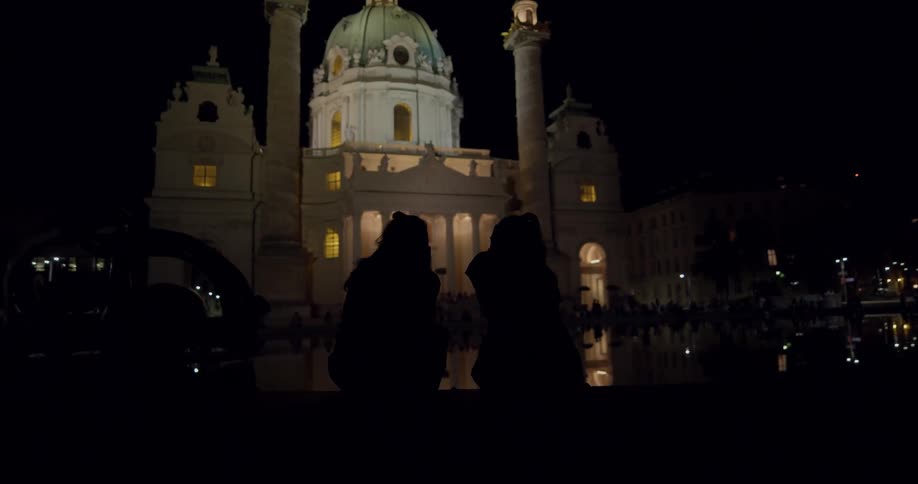Two girls sitting in front of a cathedral at night