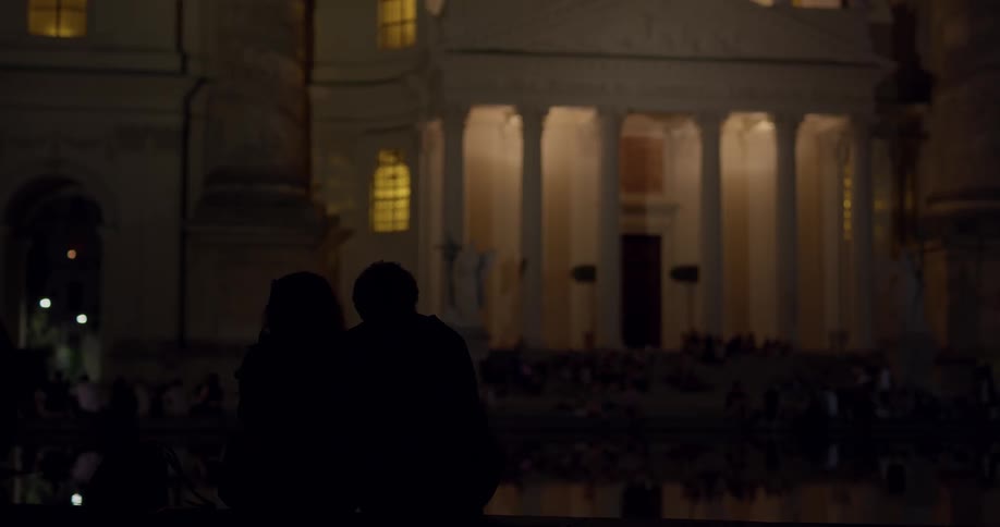 Couple sit near ornate building at night