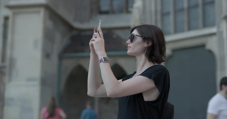 A woman stands outside taking photos then walks away