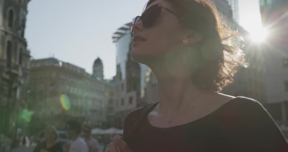 Woman wearing sunglasses walks down the city square while the sun shines