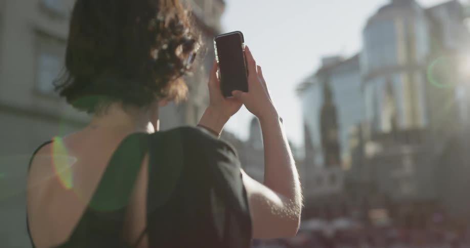 A woman uses her cell phone to take a picture of a building in the city