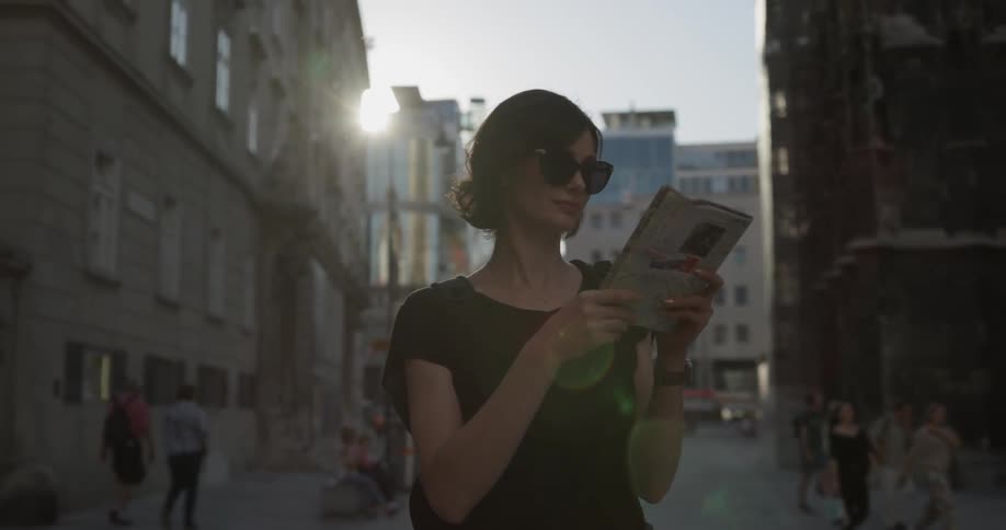 A tourist holding a guide looks up at a building and walks away