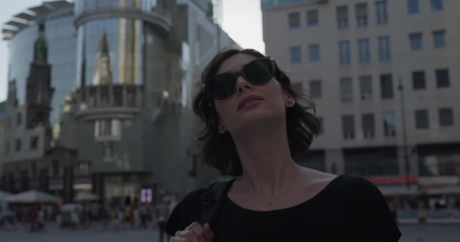 Woman wearing sunglasses looks at buildings in the city during daylight