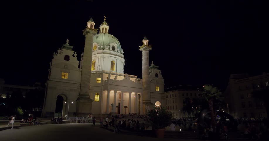 People gathered around and walking past st charles church in vienna at night