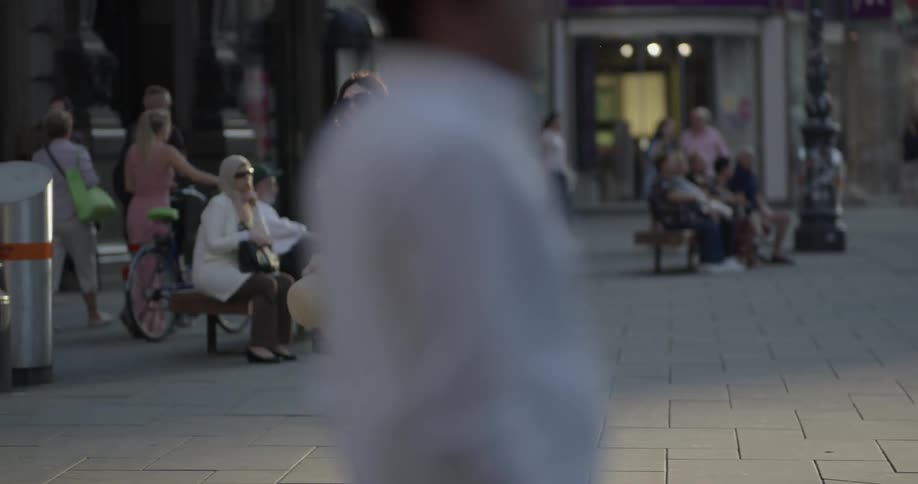 Woman wearing sunglasses walks down the city square with people background during daylight