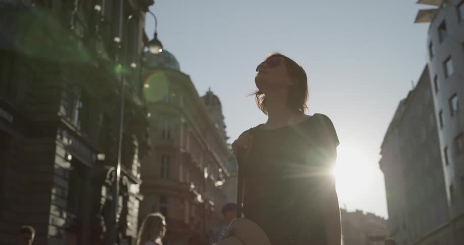 A woman holding a sun hat walks down the street while staring at the architecture
