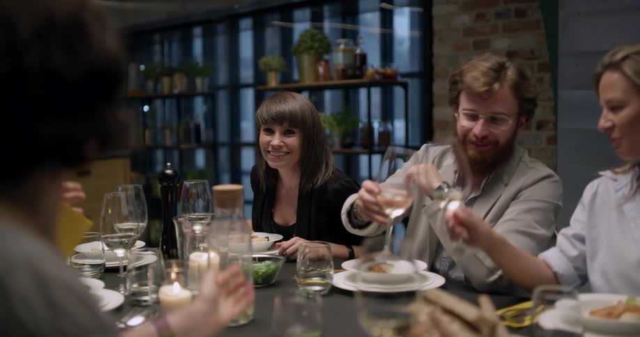 A dinner party with several people and a table full of food and drinks