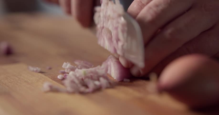 Man chops shallot on the cutting board in the kitchen during daylight