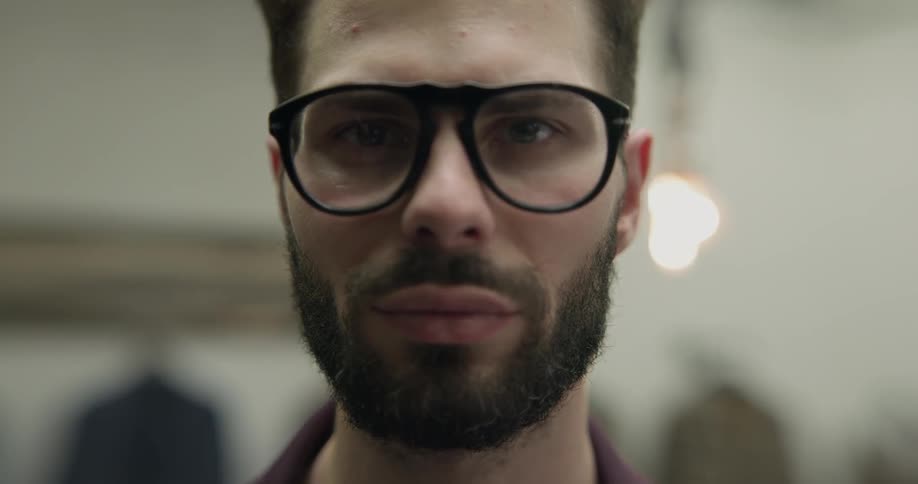 Bearded man wearing glasses lifts up head and looks at the camera indoors