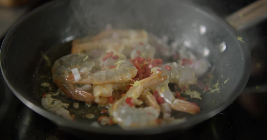 Herbs being sprinkled over a shrimp in a skillet before the skillet is shaken