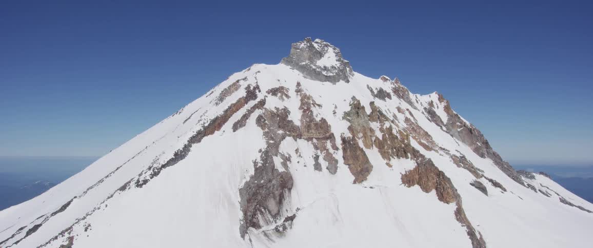 A snow covered rocky jagged mountain peak against a blue sky