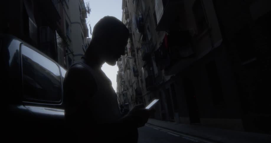 A man scrolls on a phone in a dark alley
