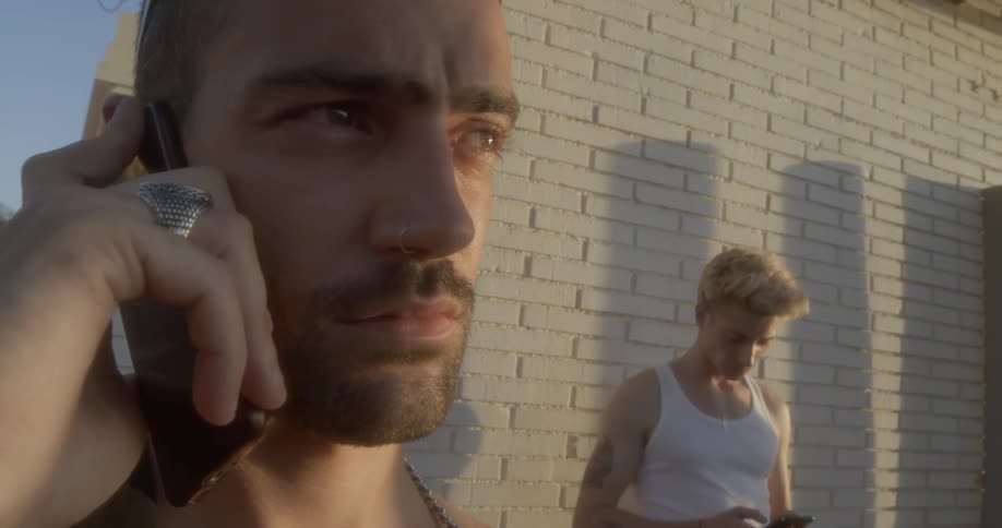 A teenager talks on a phone while another teen texts on his