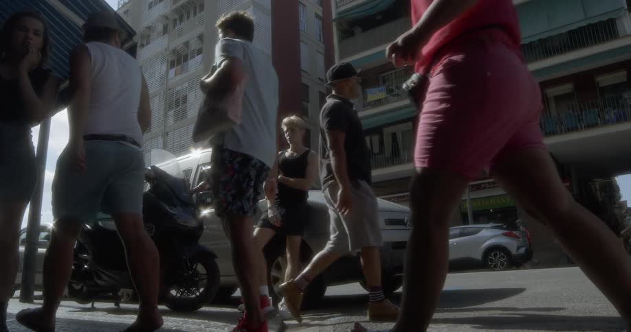 A young male smoking leaning against a vehicle as people walk past him in a busy city