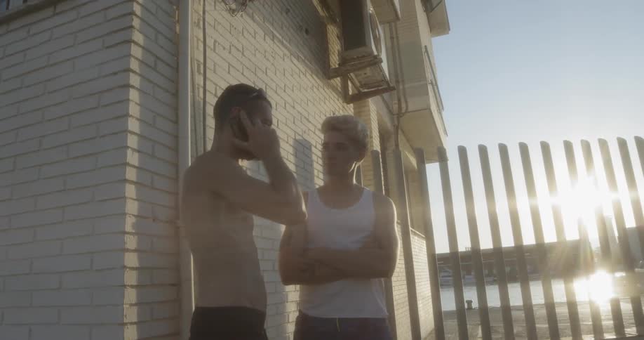 Two teenagers stand outside while one talks on the phone