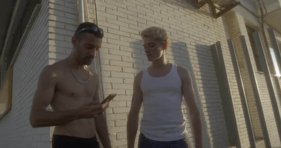 Two teenage boys stand together while one answers his phone
