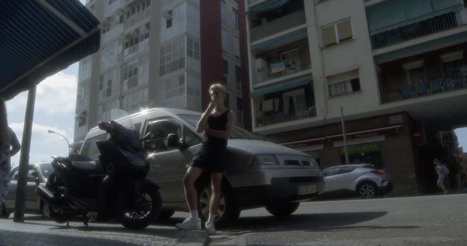 A white woman leaning against a vehicle while smoking a cigarette in a city