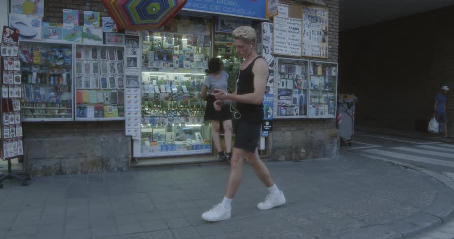 A man walks down a sidewalk outside of a crowded shop