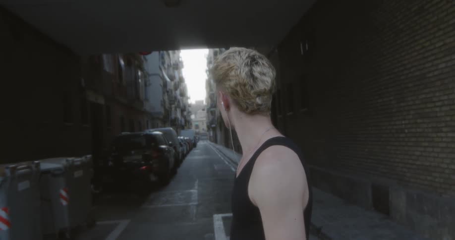 Man walking looking down a narrow street as he passes in front of it