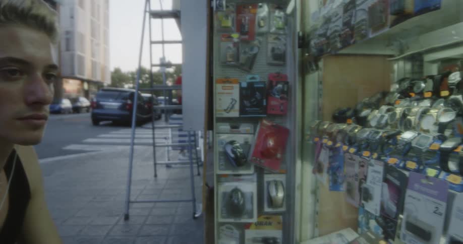 Dyed hair man looks at wrist watches window display at dusk