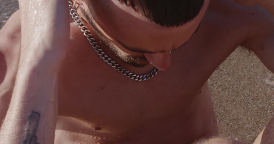 Bearded man does sit ups on the wet sand beach next to the sea