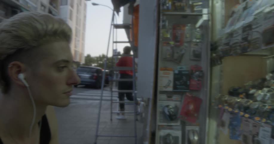 A man wearing headphones looking at a display of watches on a city street