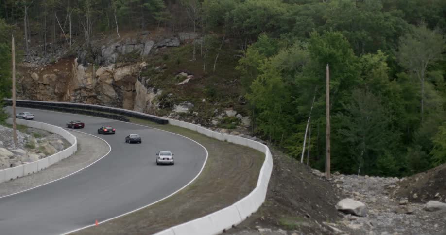 Cars are driving down a small twisting road by a cliff