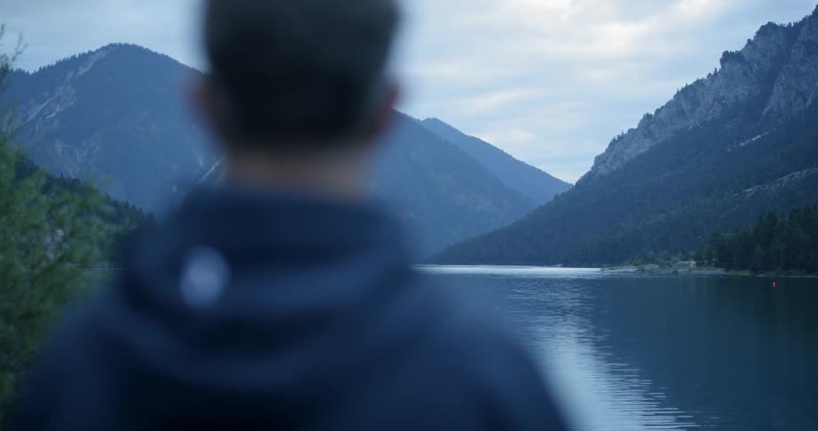 A man looks out over a lake surrounded by mountains